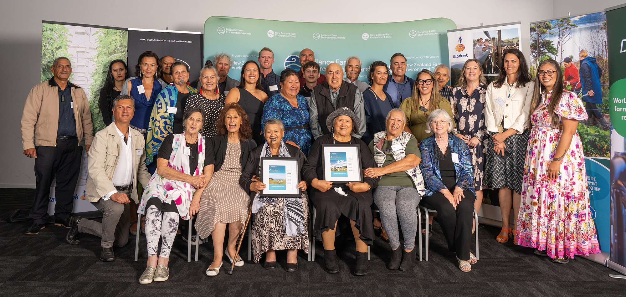 Large group of people seated and standing with two certificates.